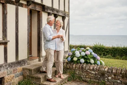 Couple de retraités devant une maison normande à colombages en bord de mer tenant les clés de leur nouveau bien immobilier